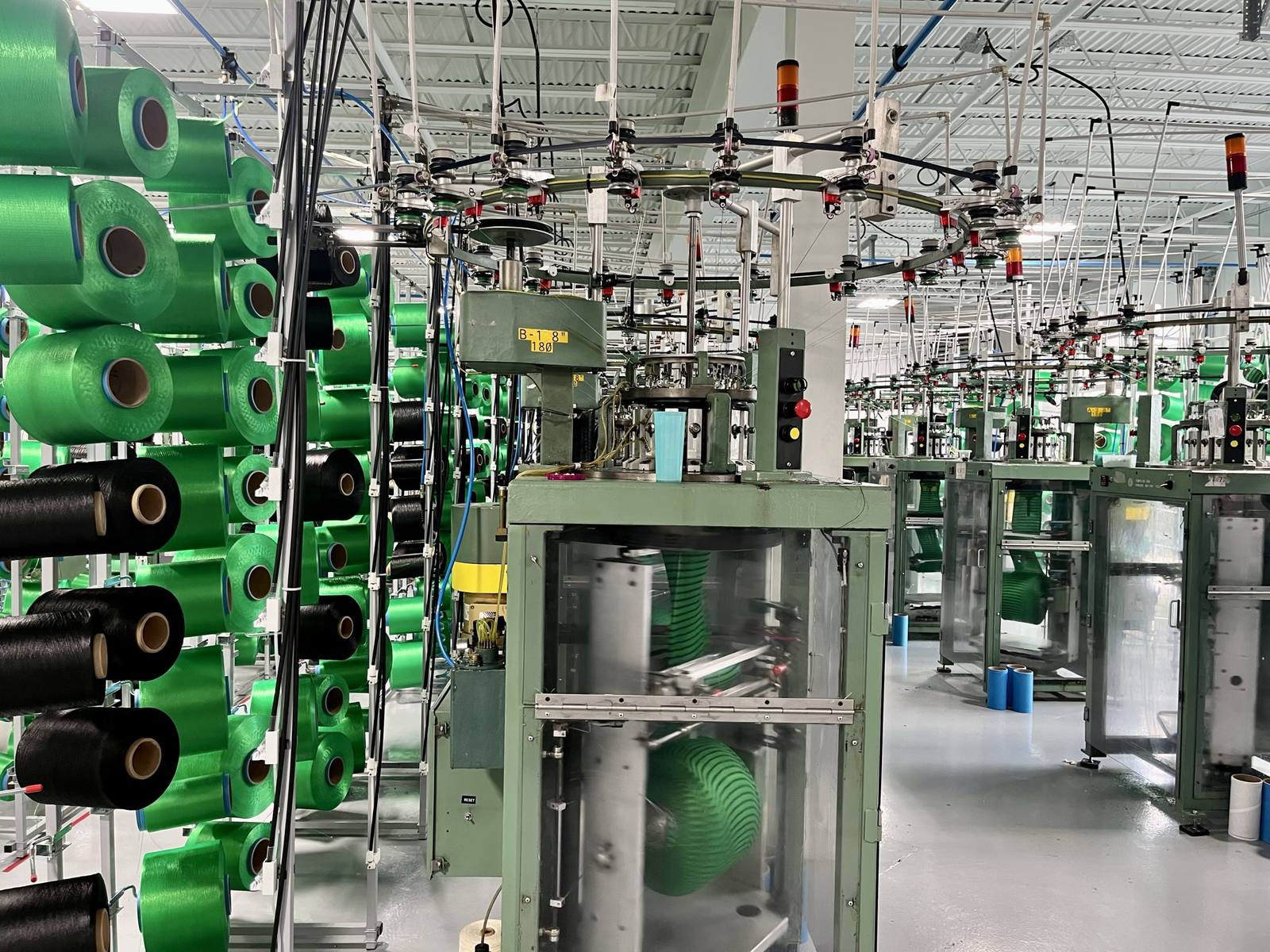 Knitting machines running green and black yarn at an MKB plant